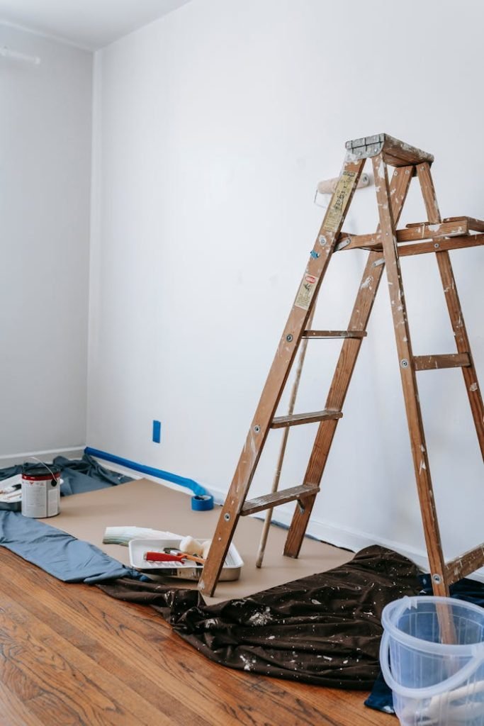 brown-wooden-stepladder-in-a-room-7217924 A home renovation scene featuring a wooden ladder, painting tools, and white walls in a room.